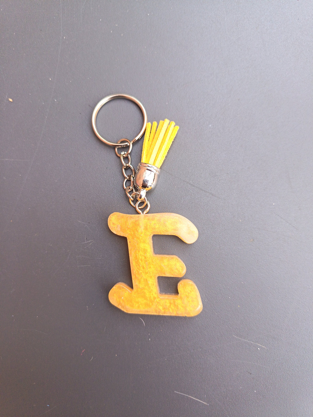 Porte-clé lettre E sculptée en résine ocre doré mat avec pompon suédine jaune moutarde et chaînette argentée