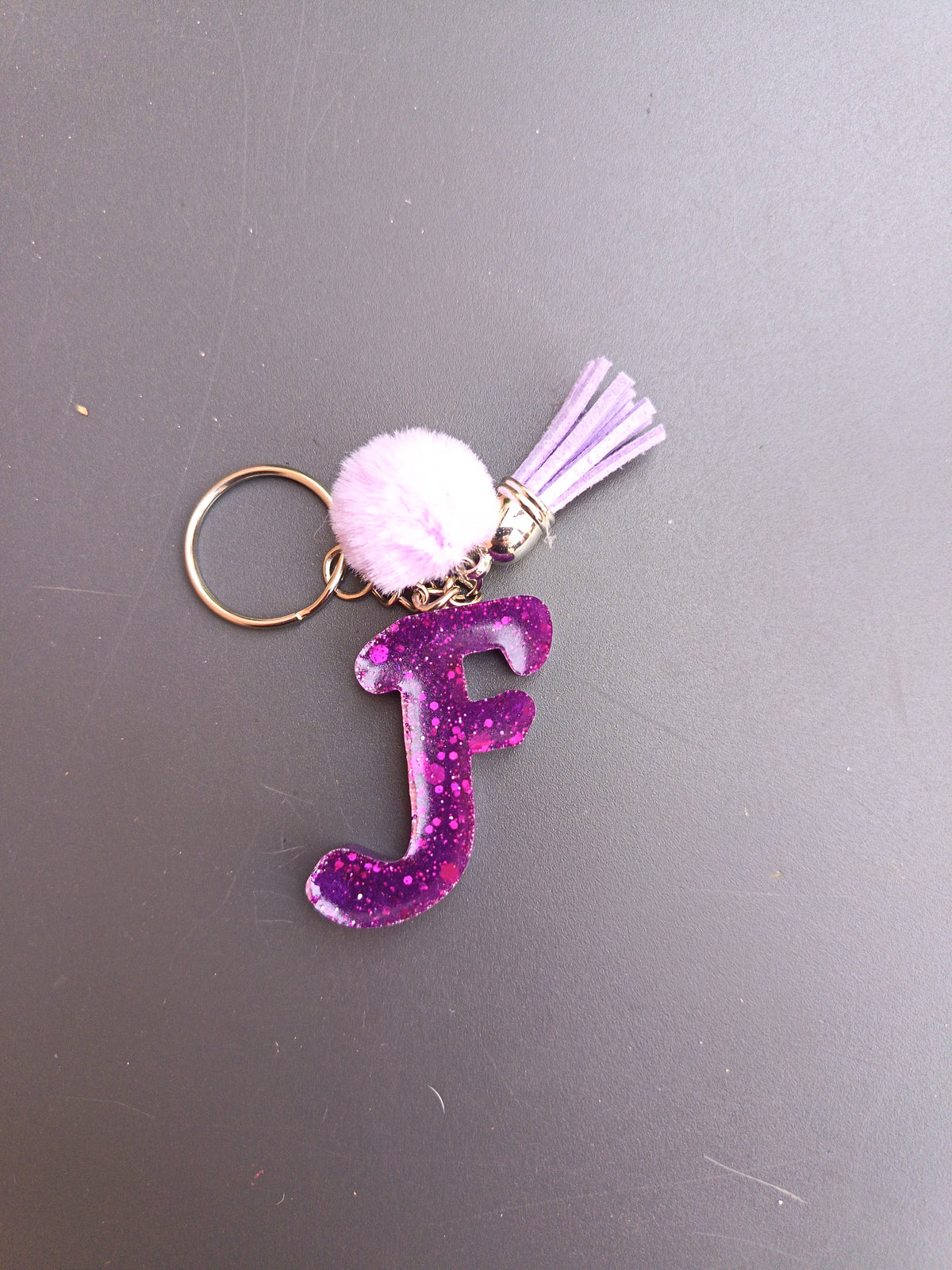 Porte-clé lettre F sculptée en résine violet fuchsia ultra-pailleté avec pompon boule fourrure rose lilas et mini-pompon suédine lilas et chaînette dorée