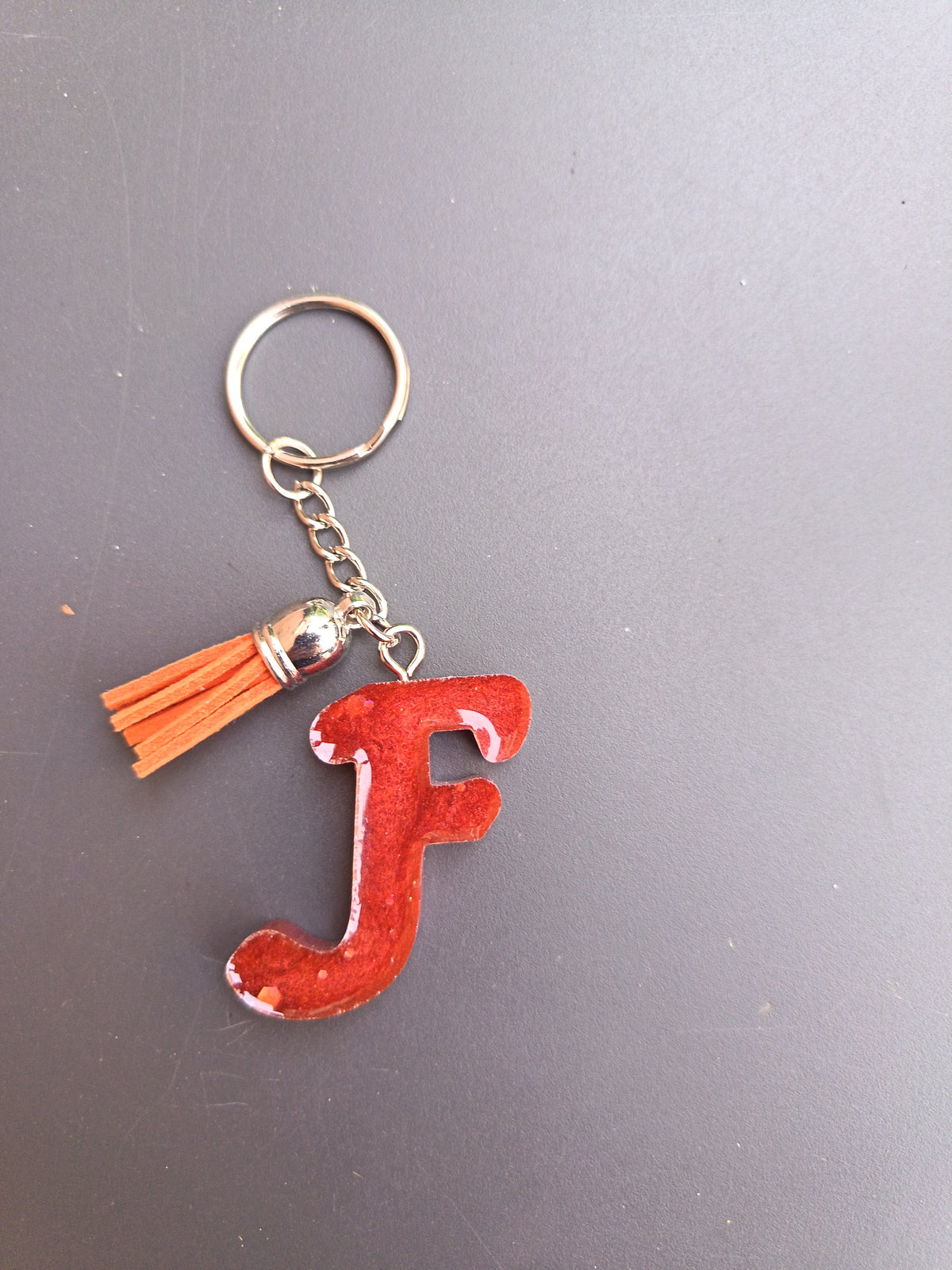 Porte-clé lettre F sculptée en résine rouge vif translucide à grosses paillettes roses et blanches avec pompon suédine orange vif et chaînette argentée