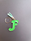 Porte-clé lettre F sculptée en résine vert fluo translucide à micro-paillettes holographiques avec pompon suédine vert menthe clair et chaînette dorée