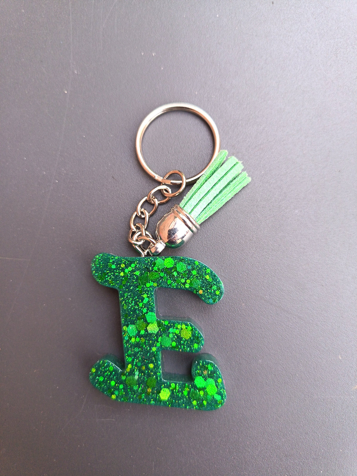 Porte-clé lettre E sculptée en résine vert forêt à grosses paillettes holographiques avec pompon suédine vert menthe clair et chaînette argentée