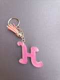 Porte-clé lettre H sculptée en résine rose bonbon translucide à micro-paillettes avec pompon suédine rose saumon et chaînette argentée
