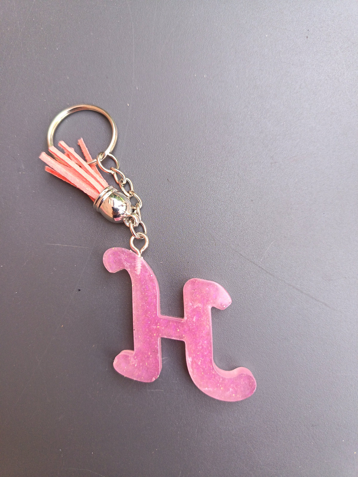 Porte-clé lettre H sculptée en résine rose bonbon translucide à micro-paillettes avec pompon suédine rose saumon et chaînette argentée