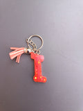 Porte-clé lettre I sculptée en résine rouge corail translucide à grosses paillettes dorées étoilées avec pompon suédine rose saumon et chaînette argentée