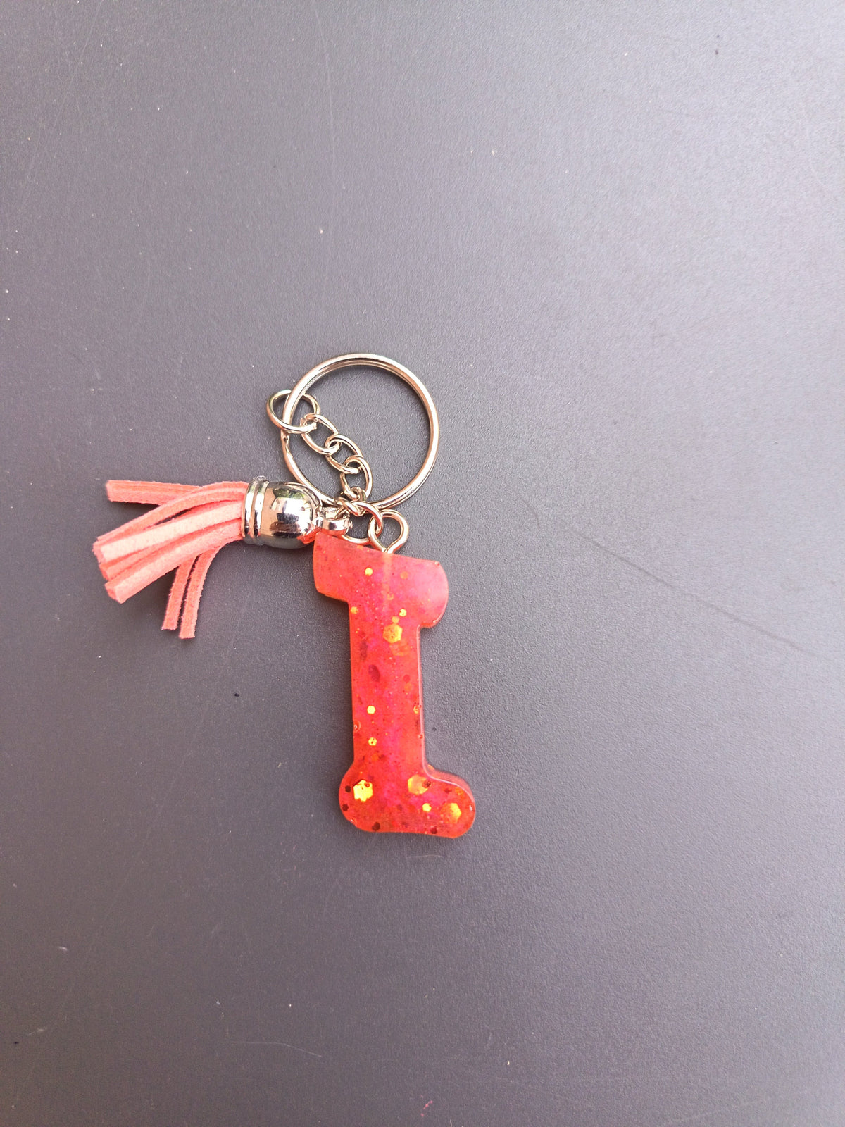 Porte-clé lettre I sculptée en résine rouge corail translucide à grosses paillettes dorées étoilées avec pompon suédine rose saumon et chaînette argentée